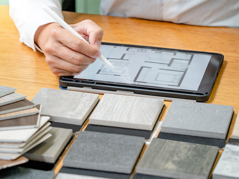 Designer wählt Feinsteinzeugfliesen und Materialmuster für modernes Innenarchitekturprojekt mit digitalem Tablet und verschiedenen Oberflächen