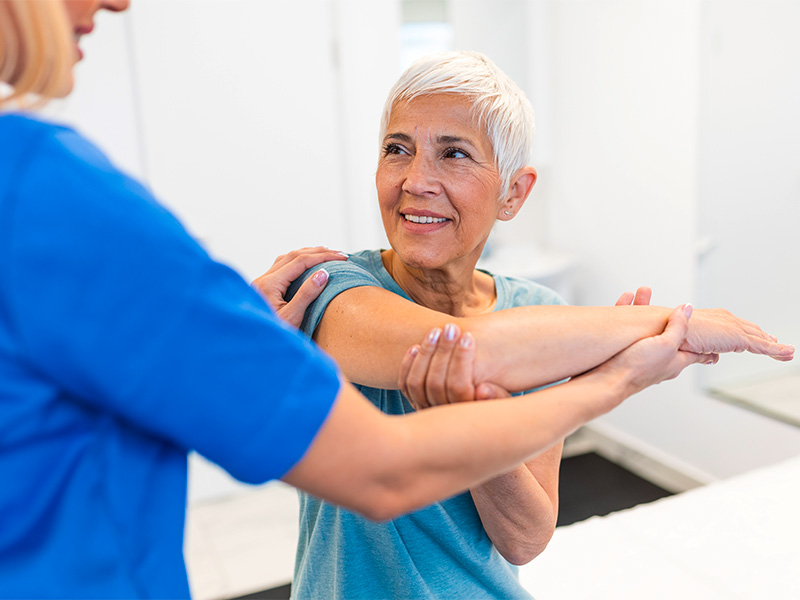 Seniorin beim Arm-Stretching unter Anleitung einer Physiotherapeutin – Rehabilitation und Schmerztherapie Physiotherapie in Kassel.