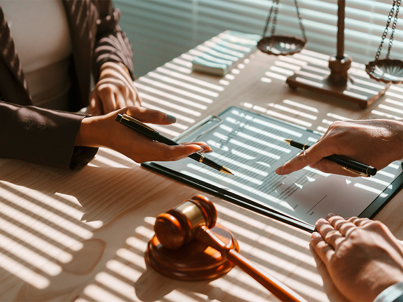 Rechtsanwalt zeigt mit Stift auf Unterschriftsfeld eines Vertragsdokuments während Besprechung im Büro, Konzentration auf rechtsverbindliche Unterschrift.