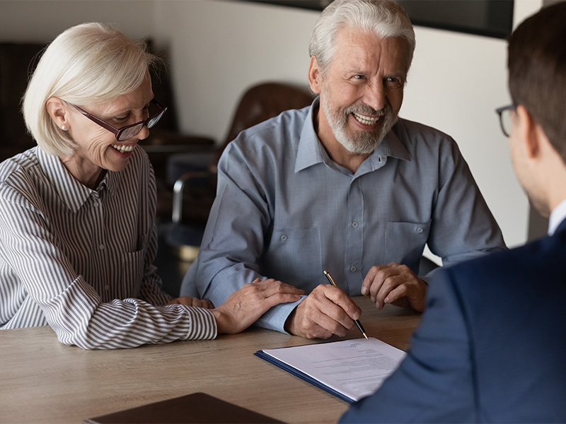 Lächelndes älteres Paar bespricht Vertragsunterzeichnung mit Rechtsberater am Tisch und erhält rechtliche Beratung zu Dokumenten.